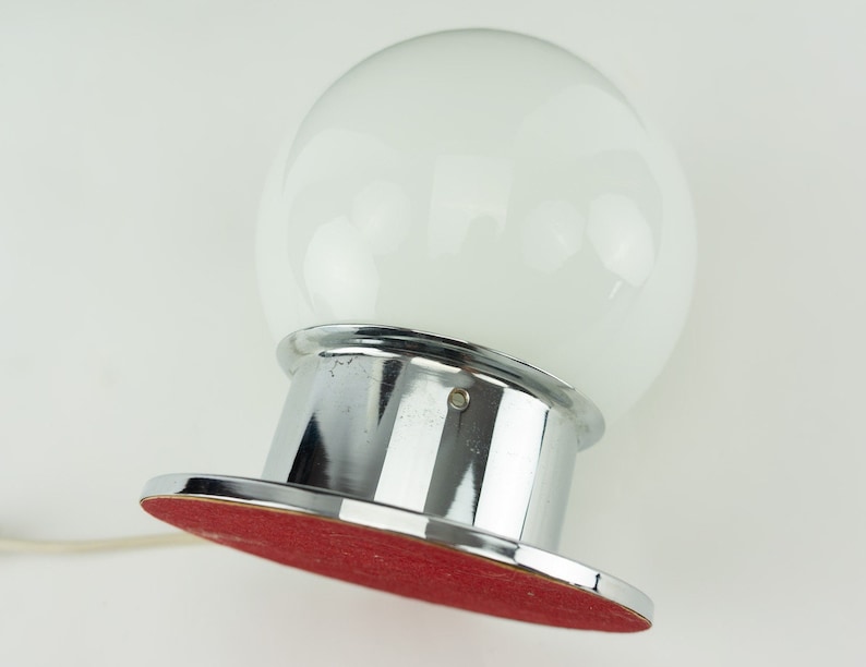 May include: A chrome table lamp with a large white glass globe shade. The base has a red felt bottom.