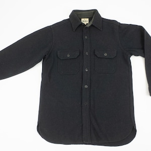 May include: A black long-sleeve shirt with two chest pockets and a button-down front. The shirt has a collared neckline and buttoned cuffs. The fabric appears to be a heavy, textured material, suitable for cooler weather.