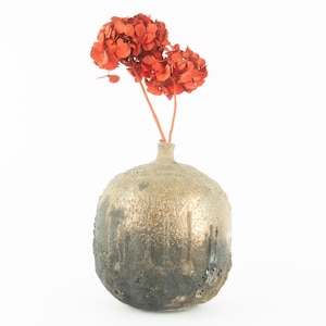 May include: A round, textured, gold and black ceramic vase with a dried orange flower arrangement.