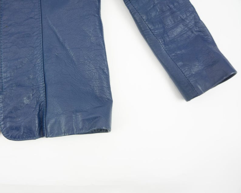 K&ouml;nnte beinhalten: Nahaufnahme eines Teils einer marineblauen Lederjacke. Das Bild zeigt die strukturierte Oberfl&auml;che des Leders und die Nahtdetails. Die Jacke scheint im Vintage- oder Retro-Stil zu sein.