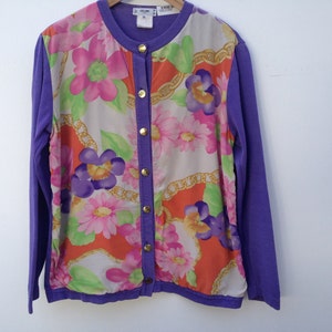 May include: A purple cardigan with a floral print on the front. The cardigan has a button closure and long sleeves.