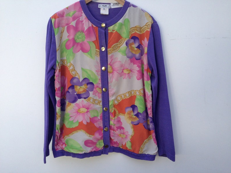 May include: A purple cardigan with a floral print on the front. The cardigan has a button closure and long sleeves.