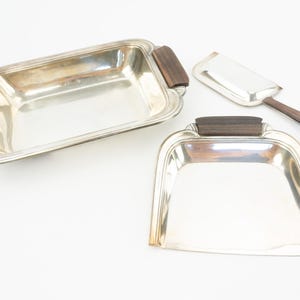 Peut inclure: Deux plateaux de service en argent avec des poignées en bois. Un plateau est rectangulaire et l'autre a la forme d'un  balai à poussière.