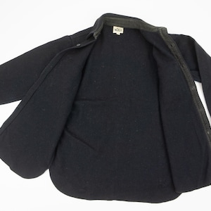 May include: A black button-down shirt with long sleeves, open to reveal the interior lining. The shirt has a collar and a small tag near the neck. The fabric appears to be a thick, warm material.