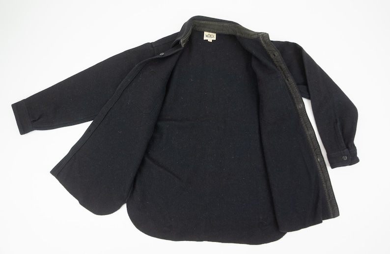 May include: A black button-down shirt with long sleeves, open to reveal the interior lining. The shirt has a collar and a small tag near the neck. The fabric appears to be a thick, warm material.