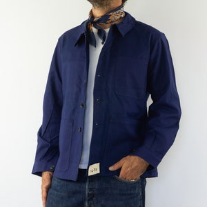 Peut inclure: Une veste de travail bleu marine avec un devant boutonné et une seule poche poitrine. La veste a une petite étiquette sur le côté inférieur gauche qui dit "DG-74".