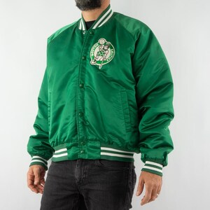 May include: A green satin baseball jacket with white stripes on the sleeves and collar. The jacket has a large embroidered patch on the left chest featuring a basketball player and the words "Boston Celtics".