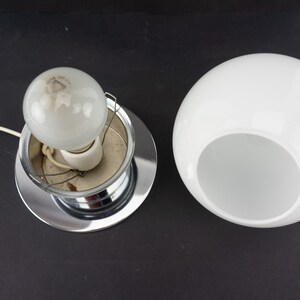 May include: A chrome ceiling light fixture with a white glass shade. The shade has a hole in the bottom to allow light to shine through.