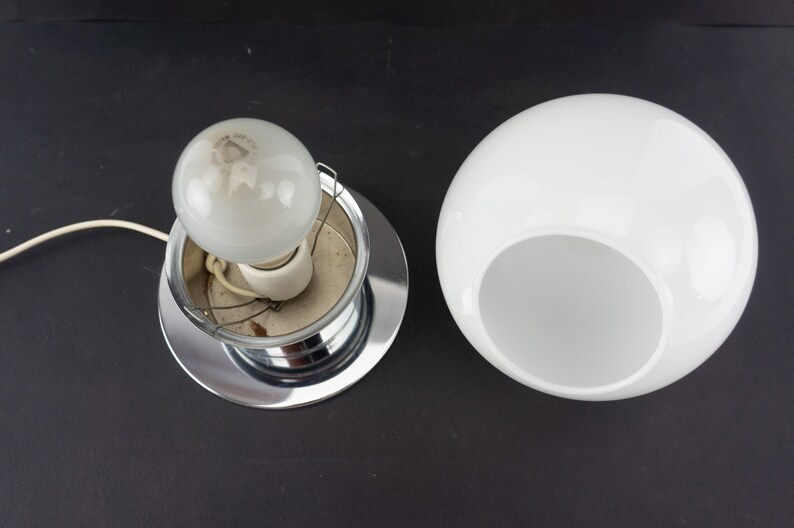 May include: A chrome ceiling light fixture with a white glass shade. The shade has a hole in the bottom to allow light to shine through.