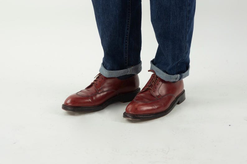 May include: A pair of brown leather lace-up shoes with a pointed toe. The shoes are worn with rolled up blue jeans.