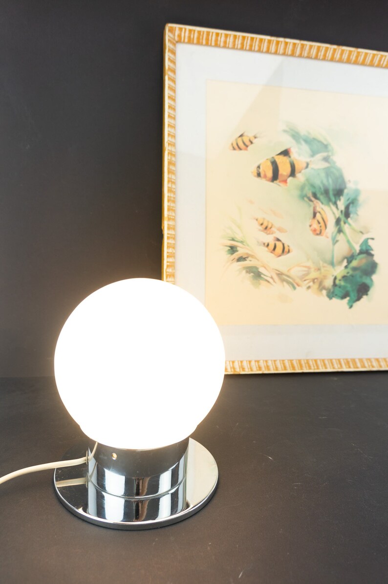May include: A chrome table lamp with a white glass globe shade. The lamp is turned on and the globe is illuminated.