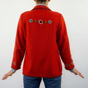May include: A red wool blazer with embroidered flowers on the back and sleeves. The blazer has a black trim around the edges.