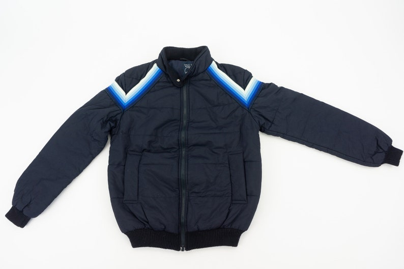 May include: A navy blue puffer jacket with a zipper closure and a white and blue chevron design on the shoulders.