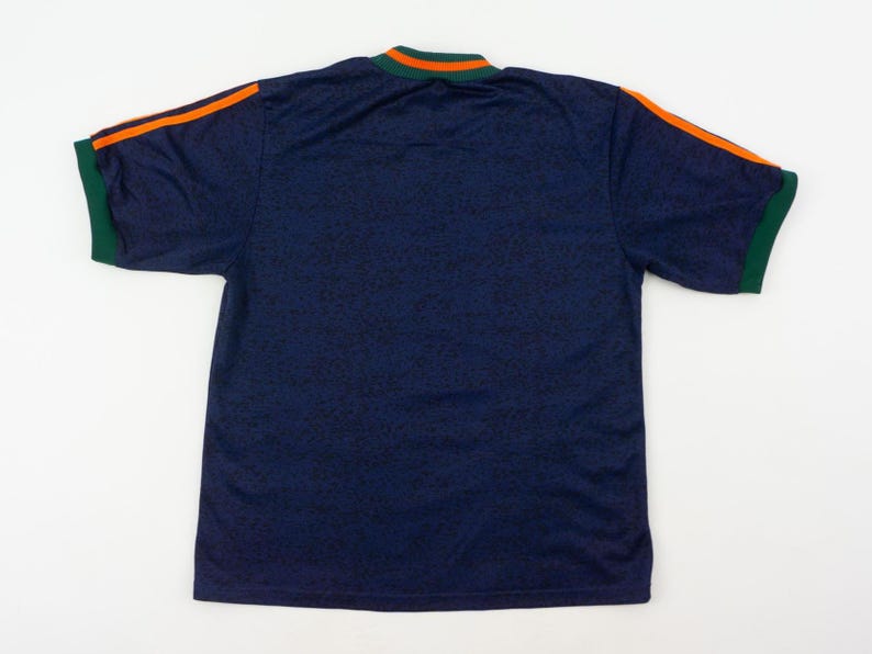 May include: Navy blue short-sleeve shirt with orange stripes on the shoulders and green trim on the sleeves and collar. The shirt has a subtle pattern throughout the fabric.