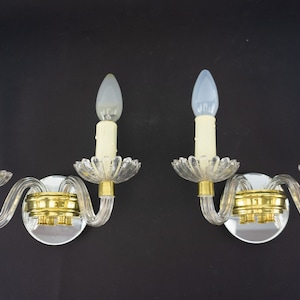 May include: A pair of crystal wall sconces with clear glass arms and gold accents. Each sconce has two candle-style light bulbs.