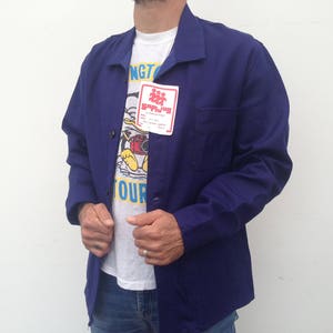 May include: A dark blue work jacket with a white t-shirt underneath. The t-shirt has a cartoon character and the text "Sapijoy" on it.