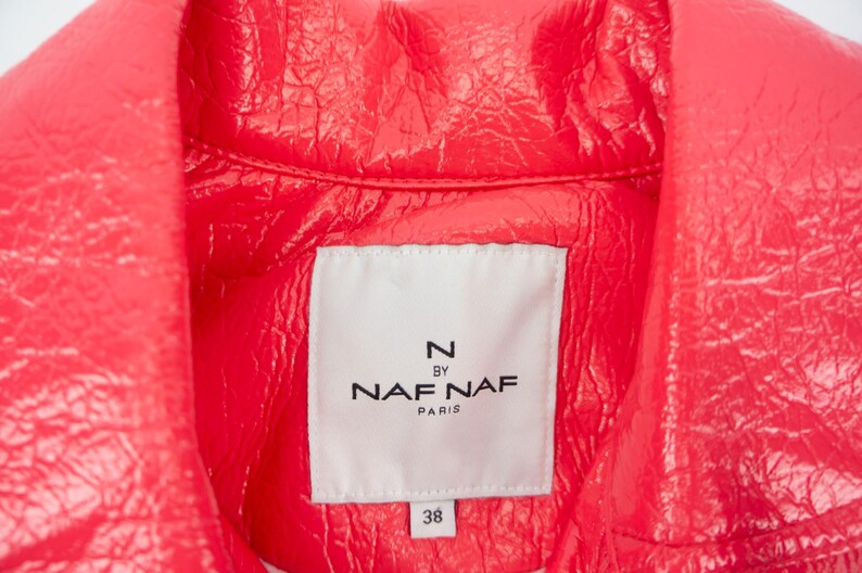 May include: Close-up of a bright pink leather jacket with a white label that reads "N by Naf Naf Paris" and "38".