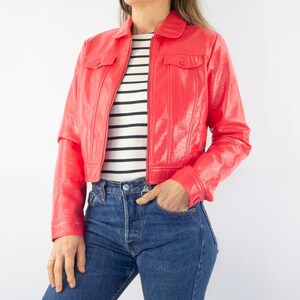 May include: A cropped red leather jacket with a zipper closure and two flap pockets. The jacket has a shiny finish and a collar.