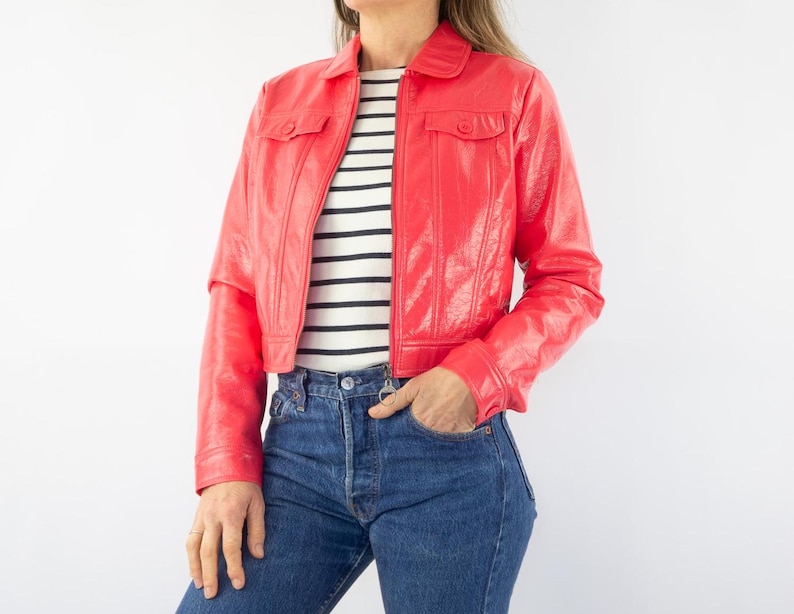May include: A cropped red leather jacket with a zipper closure and two flap pockets. The jacket has a shiny finish and a collar.