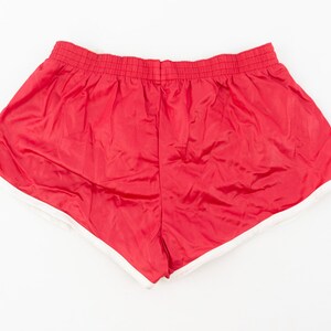 May include: Red athletic shorts with a white trim around the leg openings. The shorts have an elastic waistband.