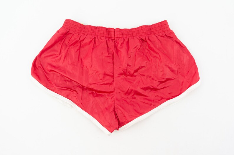 May include: Red athletic shorts with a white trim around the leg openings. The shorts have an elastic waistband.