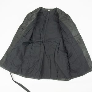 May include: A black jacket with a button-up front and a tie closure. The jacket is open, revealing a black lining. The garment appears to be made of a leather or leather-like material.