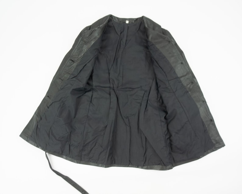 May include: A black jacket with a button-up front and a tie closure. The jacket is open, revealing a black lining. The garment appears to be made of a leather or leather-like material.