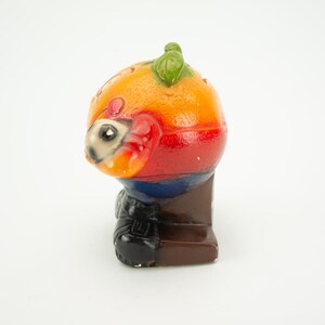 May include: A colorful ceramic figurine of a person wearing a red, orange, yellow, blue, and black outfit. The figurine is standing on a brown base.