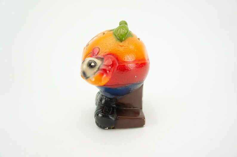 May include: A colorful ceramic figurine of a person wearing a red, orange, yellow, blue, and black outfit. The figurine is standing on a brown base.