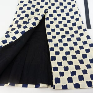 May include: A white skirt with a blue and white checkered pattern. The skirt has a slit up the front and a black belt.
