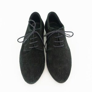 Op de afbeelding: Een paar zwarte su&egrave;de veterschoenen met een geperforeerd ontwerp.