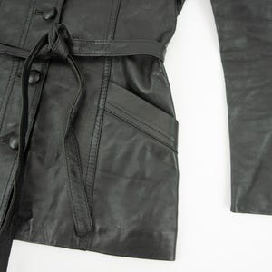 May include: Black leather jacket with a belted waist, button closures, and a pocket. The jacket has long sleeves and a tailored fit. The leather appears to be slightly distressed.