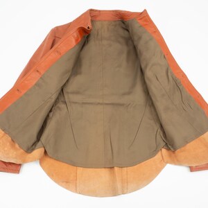 May include: Open orange leather jacket with a brown interior lining. The jacket has a classic collar and button closures. The interior features a soft, suede-like texture.