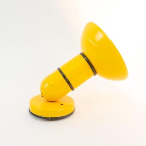 Può includere: Una lampada da scrivania giallo brillante con un paralume arrotondato e un corpo cilindrico. La lampada ha una base circolare ed è accentuata da anelli neri. Il design è moderno e minimalista, adatta per una scrivania o un comodino.