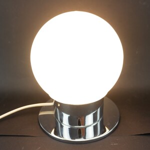 May include: A chrome table lamp with a white glass globe shade. The lamp has a round base and a cord.