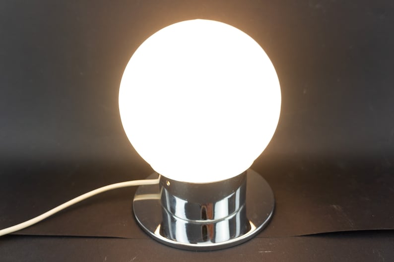May include: A chrome table lamp with a white glass globe shade. The lamp has a round base and a cord.