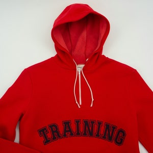 K&ouml;nnte beinhalten: Roter Kapuzenpullover mit einem schwarzen gestickten "TRAINING"-Motiv auf der Vorderseite.