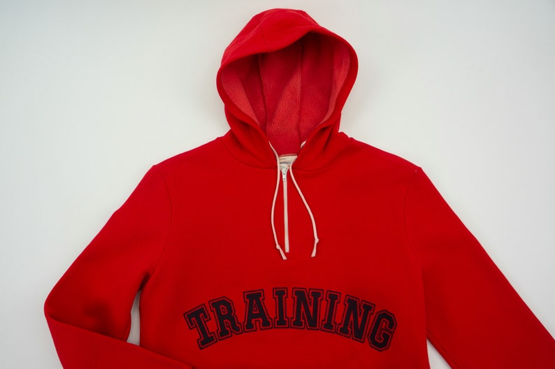 K&ouml;nnte beinhalten: Roter Kapuzenpullover mit einem schwarzen gestickten "TRAINING"-Motiv auf der Vorderseite.