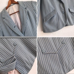 Puede incluir: Una chaqueta azul claro con rayas blancas. La chaqueta tiene cierre de doble botonadura con botones y un bolsillo en el lado izquierdo.