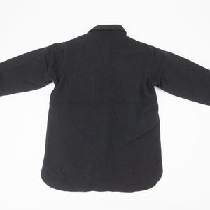 May include: A black, long-sleeved shirt jacket with a button-down front and collar. The jacket has buttoned cuffs and a rounded hem. The garment is displayed on a white background.