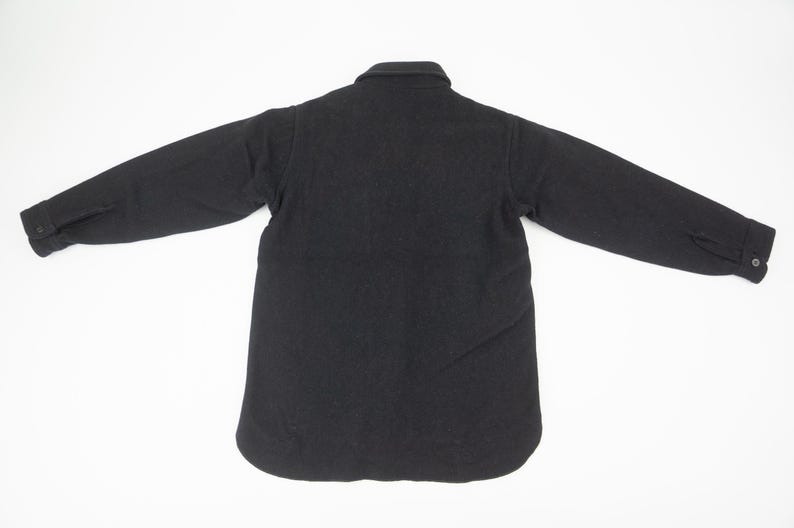 May include: A black, long-sleeved shirt jacket with a button-down front and collar. The jacket has buttoned cuffs and a rounded hem. The garment is displayed on a white background.