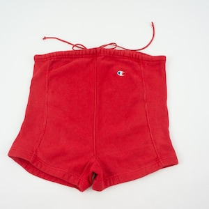 May include: Red Champion shorts with a drawstring waist. The shorts feature the Champion logo in white, blue, and red. The shorts are made of a soft material and are suitable for athletic activities.