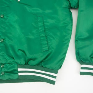 May include: Green satin bomber jacket with white and green striped cuffs and waistband. The jacket has a button closure and a pocket on the left side.