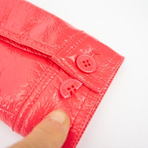 May include: Close-up of a bright pink jacket with two red buttons on the sleeve.