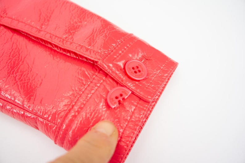 May include: Close-up of a bright pink jacket with two red buttons on the sleeve.