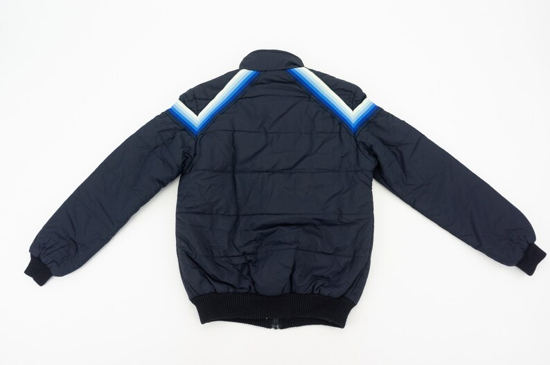 May include: A navy blue puffer jacket with a white and blue striped design on the shoulders.