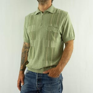 May include: A short-sleeved sage green knit polo shirt featuring a quarter-zip neckline, a small chest pocket, and a vertical textured stripe pattern. The garment has a ribbed collar, sleeve cuffs, and a ribbed hemline for a structured fit.