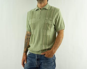 May include: A short-sleeved sage green knit polo shirt featuring a quarter-zip neckline, a small chest pocket, and a vertical textured stripe pattern. The garment has a ribbed collar, sleeve cuffs, and a ribbed hemline for a structured fit.