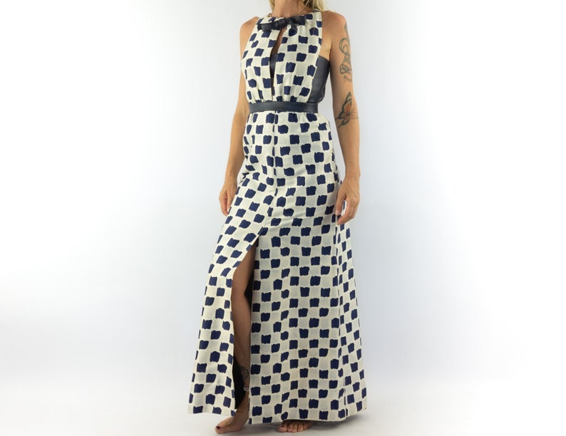 May include: A white maxi dress with a black belt and a blue and white checkered pattern. The dress has a keyhole neckline and a slit up the front.