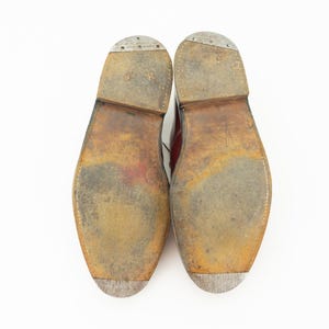 May include: Close-up of the soles of a pair of brown leather shoes. The soles are worn and have a textured pattern.